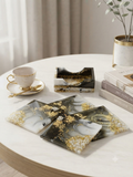 Set of 4 handmade black white and grey marble swirl resin coasters with gold leaf, displayed with matching resin holder on a white marble coffee table with a gold-rimmed tea cup