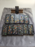 Handmade black resin domino set with holographic multicolour star glitter and grey pearl dots, displayed on a grey velvet pouch with a wooden box holder, arranged in rows